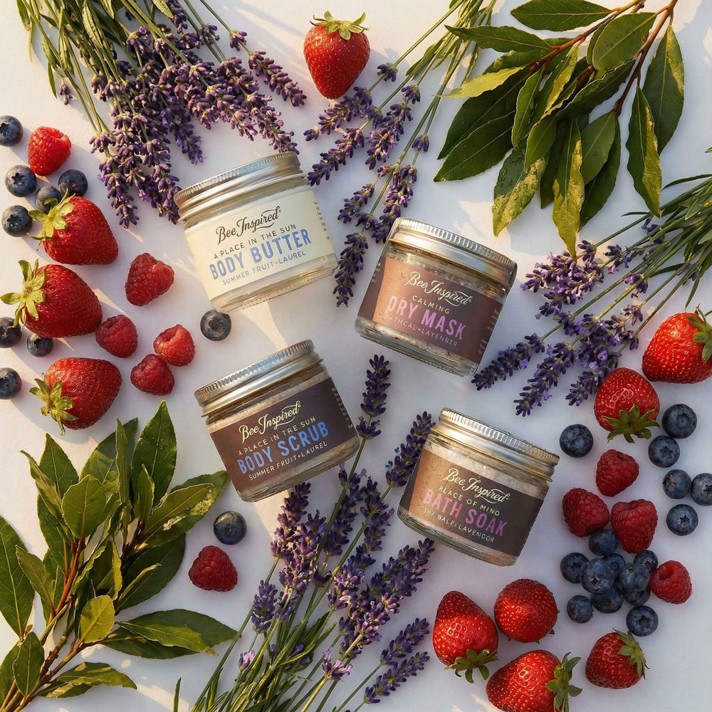 Four jars of body care products surrounded by strawberries, lavender, and blueberries on a white background.