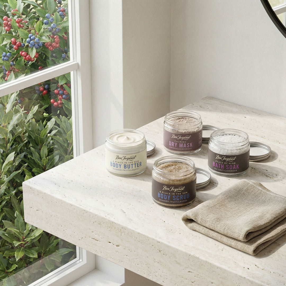 Set of skincare products including body butter, scrub, and mask on a windowsill with plants in the background.