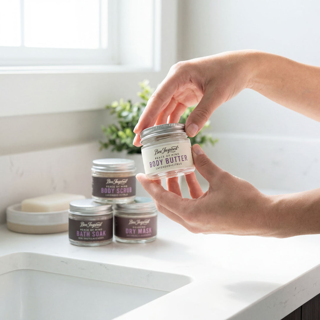 Person holding a jar of body butter with other skincare products on a counter.