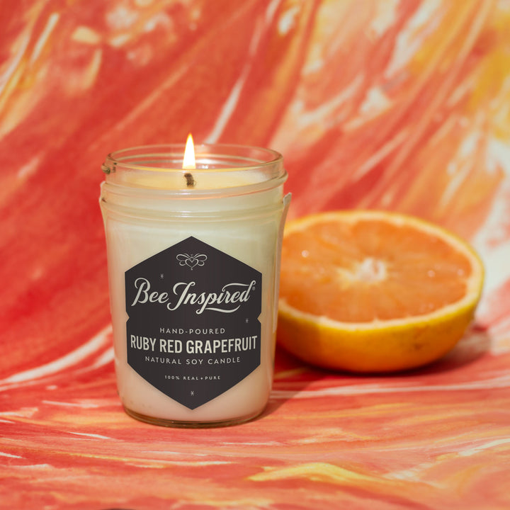 Ruby Red Grapefruit jelly jar candle burning against red and orange art 