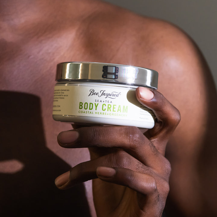 Hand holding a jar of 'Bee Inspired' body cream against a blurred background