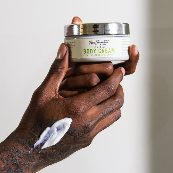 Hand holding a jar of 'Bee & Tallow' body cream with visible cream on the palm.