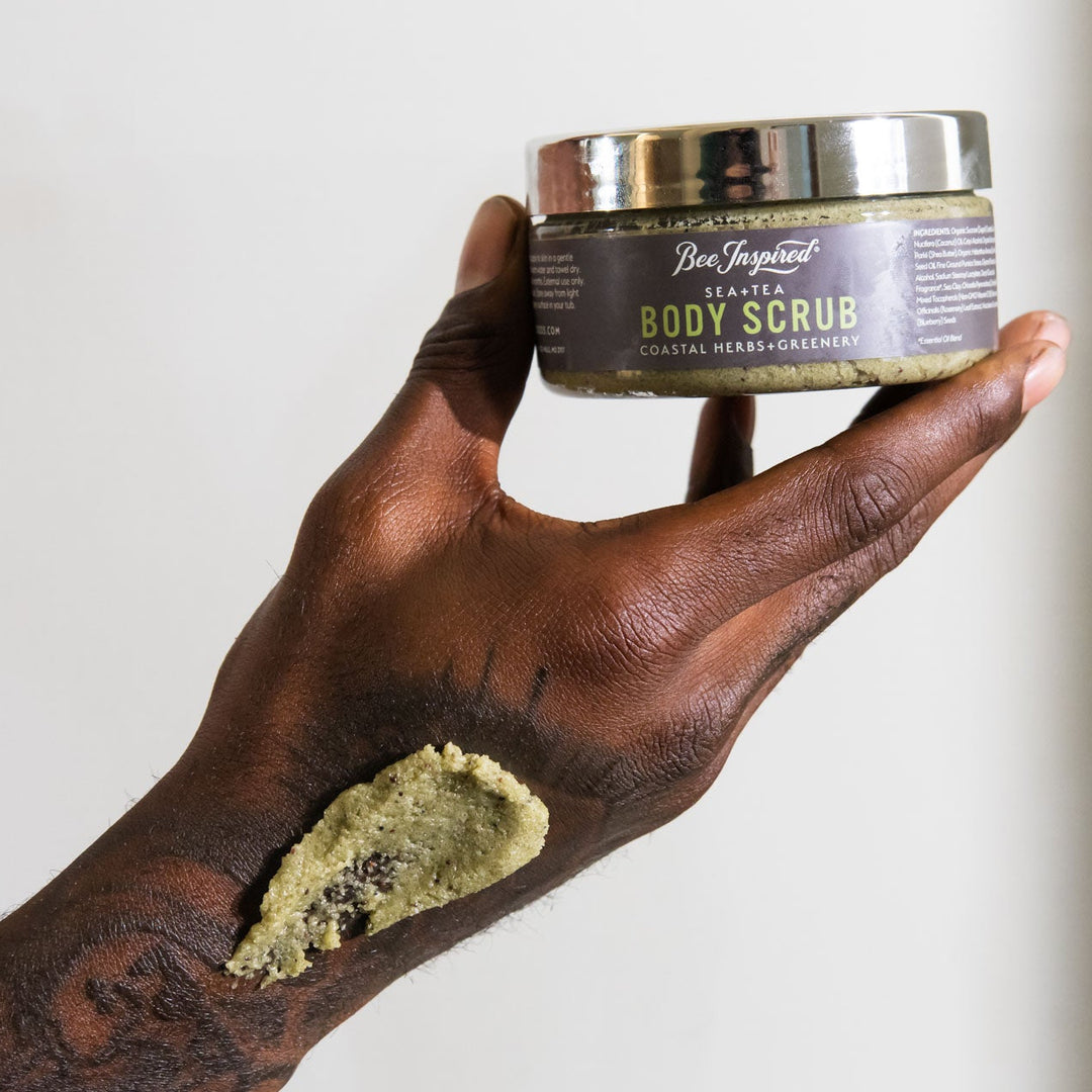 Hand holding a jar of body scrub with visible product on skin against a neutral background