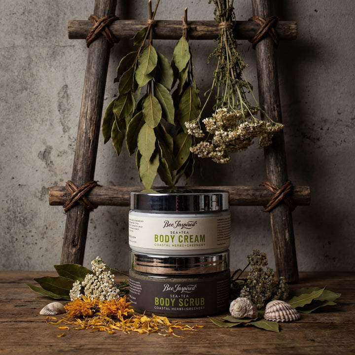 Two containers of 'Bee Inspired' body care products on a wooden surface with plants and natural elements.