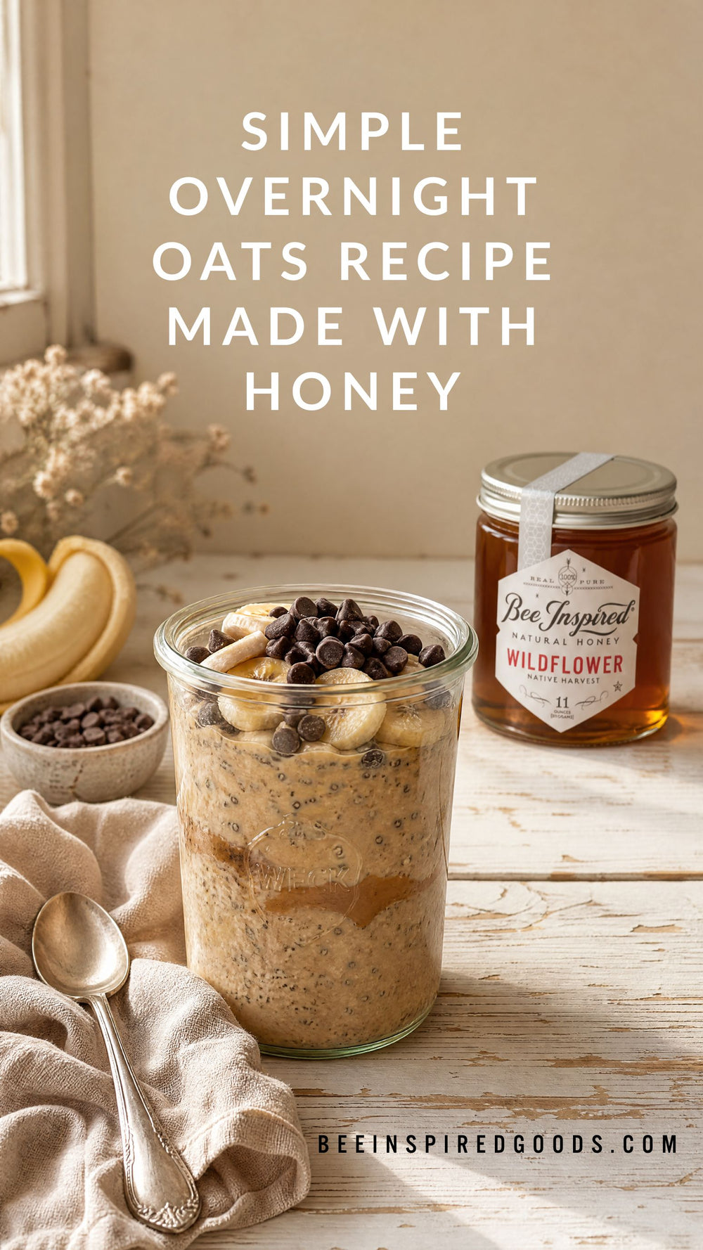 Overnight oats in a clear glass jar topped with banana slices and chocolate chips, set on a wooden table beside a jar of Bee Inspired Goods Wildflower honey, with text reading 'SIMPLE OVERNIGHT OATS RECIPE MADE WITH HONEY'.