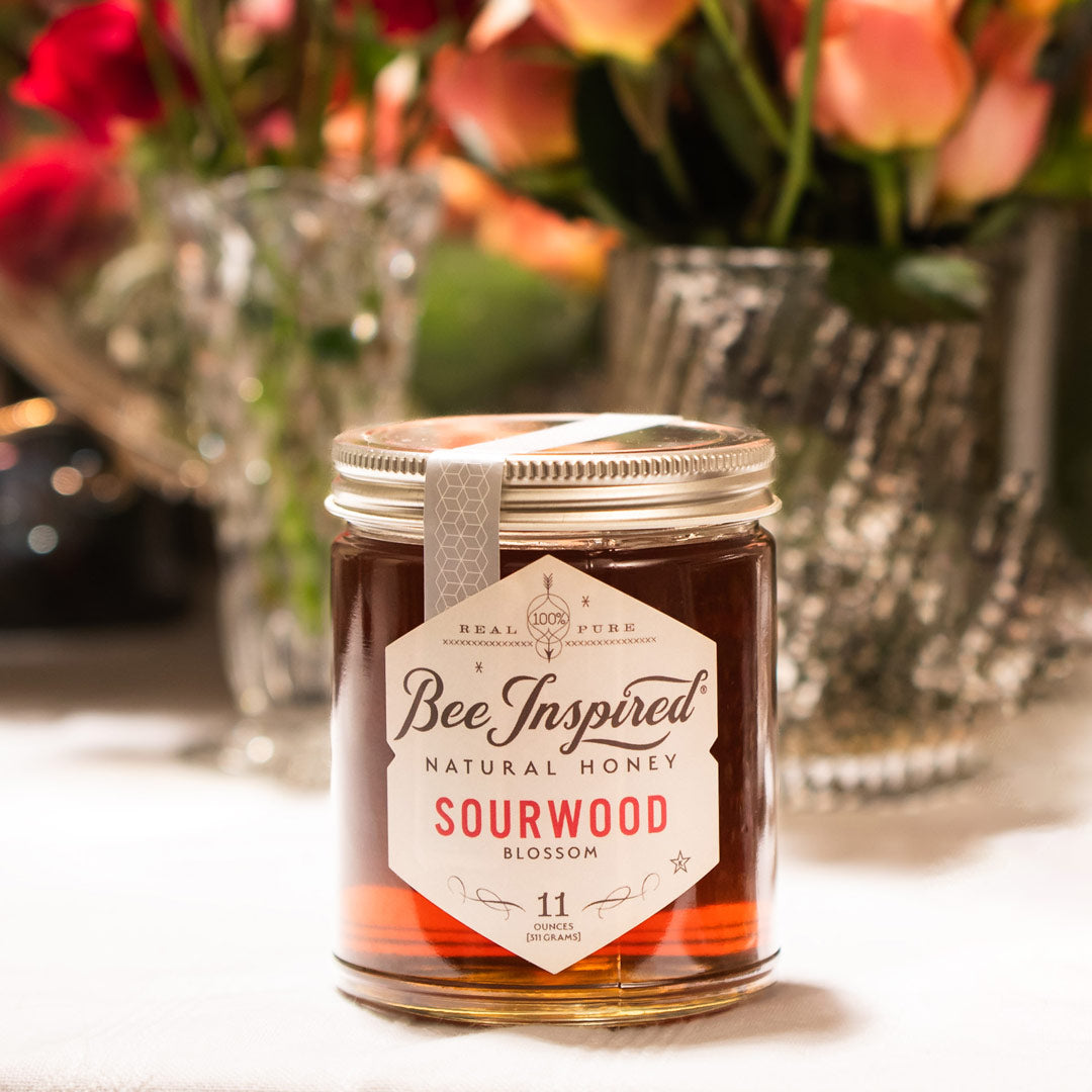 Jar of Bee Inspired sourwood honey with flowers in the background