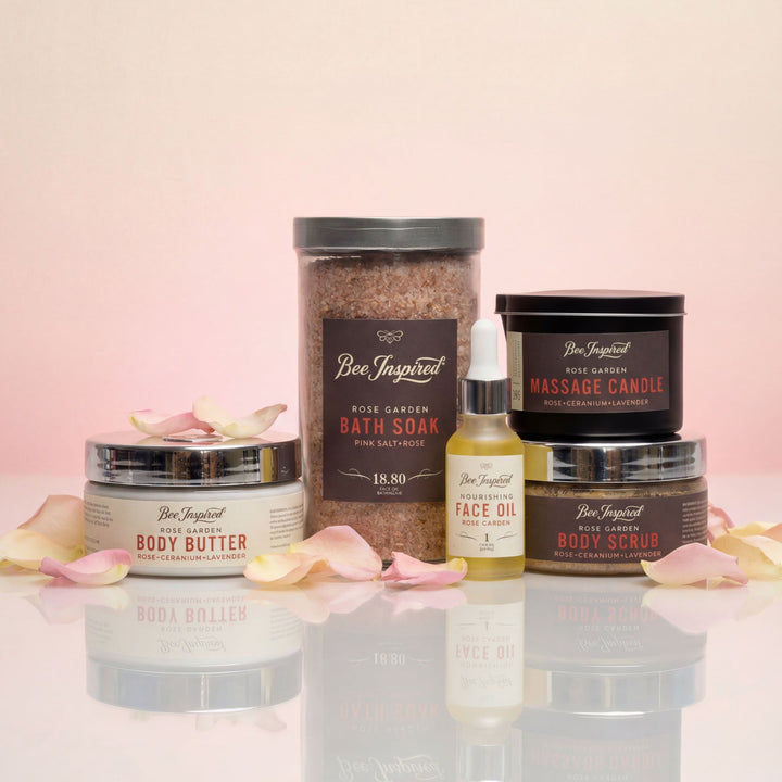 Collection of Bee Inspired skincare and body care products on a reflective surface with a pink background.