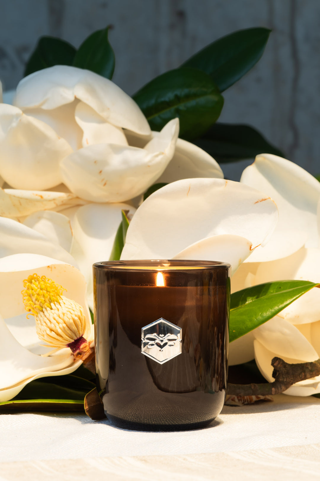 Luxe candle burning in front of white magnolia flowers 