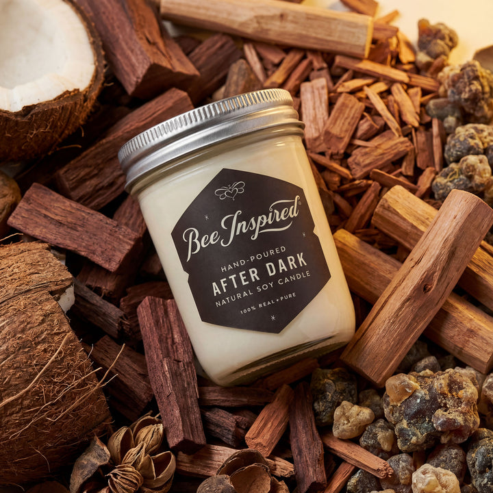 Candle jar labeled 'Bee Inspired' surrounded by wood chips and coconuts