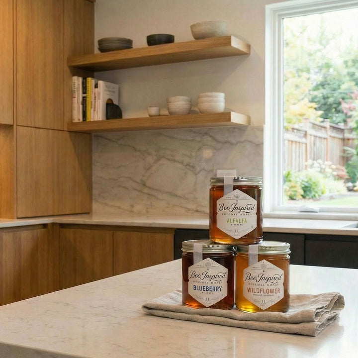 Three jars of honey labeled 'Bee Inspired' on a kitchen counter with a window in the background.