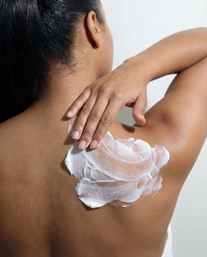 Person applying white cream to their shoulder against a neutral background