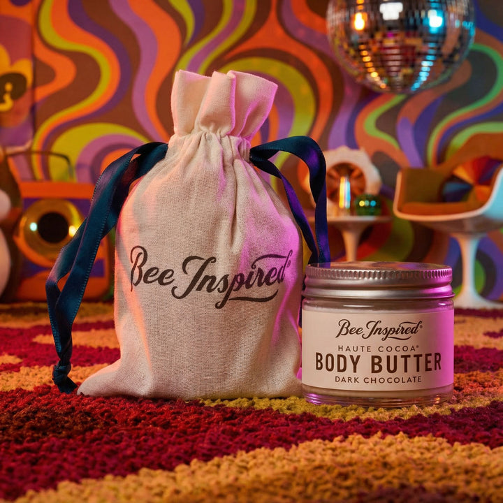 Bee Inspired body butter jar with a drawstring bag against a colorful, retro-style background.