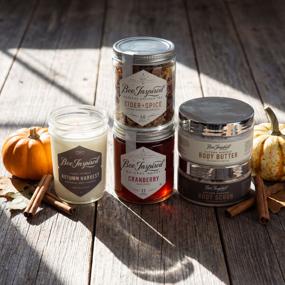 Collection of Bee Inspired products including candles and honey on a wooden surface with pumpkins and cinnamon sticks.