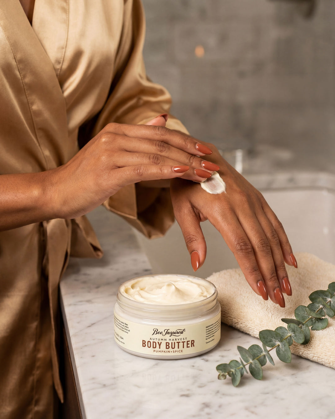 Person applying body butter to their hand with a jar of body butter on a marble surface.