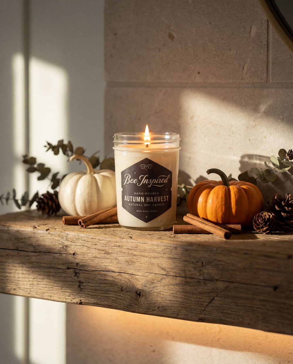 Candle labeled 'Bee Inspired Autumn Harvest' on a wooden surface with pumpkins and cinnamon sticks.