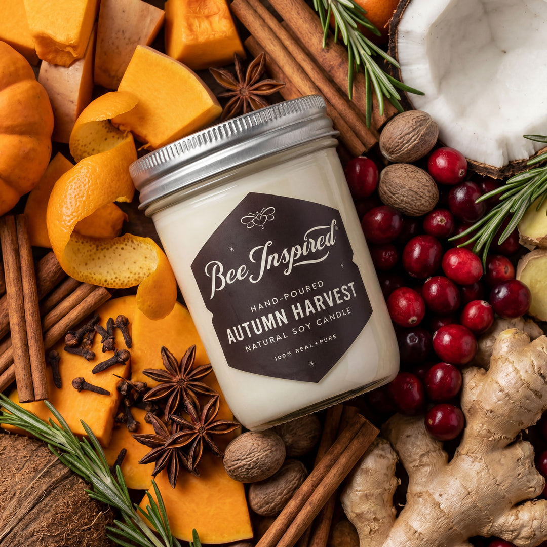 Candle labeled 'Bee Inspired' surrounded by autumnal ingredients like pumpkins, cranberries, and spices.