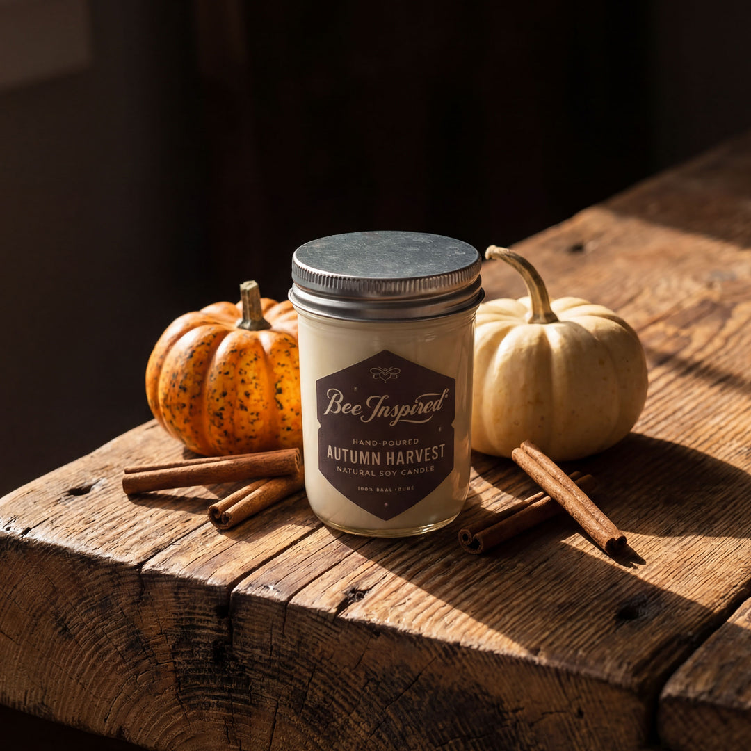 Candle labeled 'Bee Inspired Autumn Harvest' on a wooden surface with pumpkins and cinnamon sticks.
