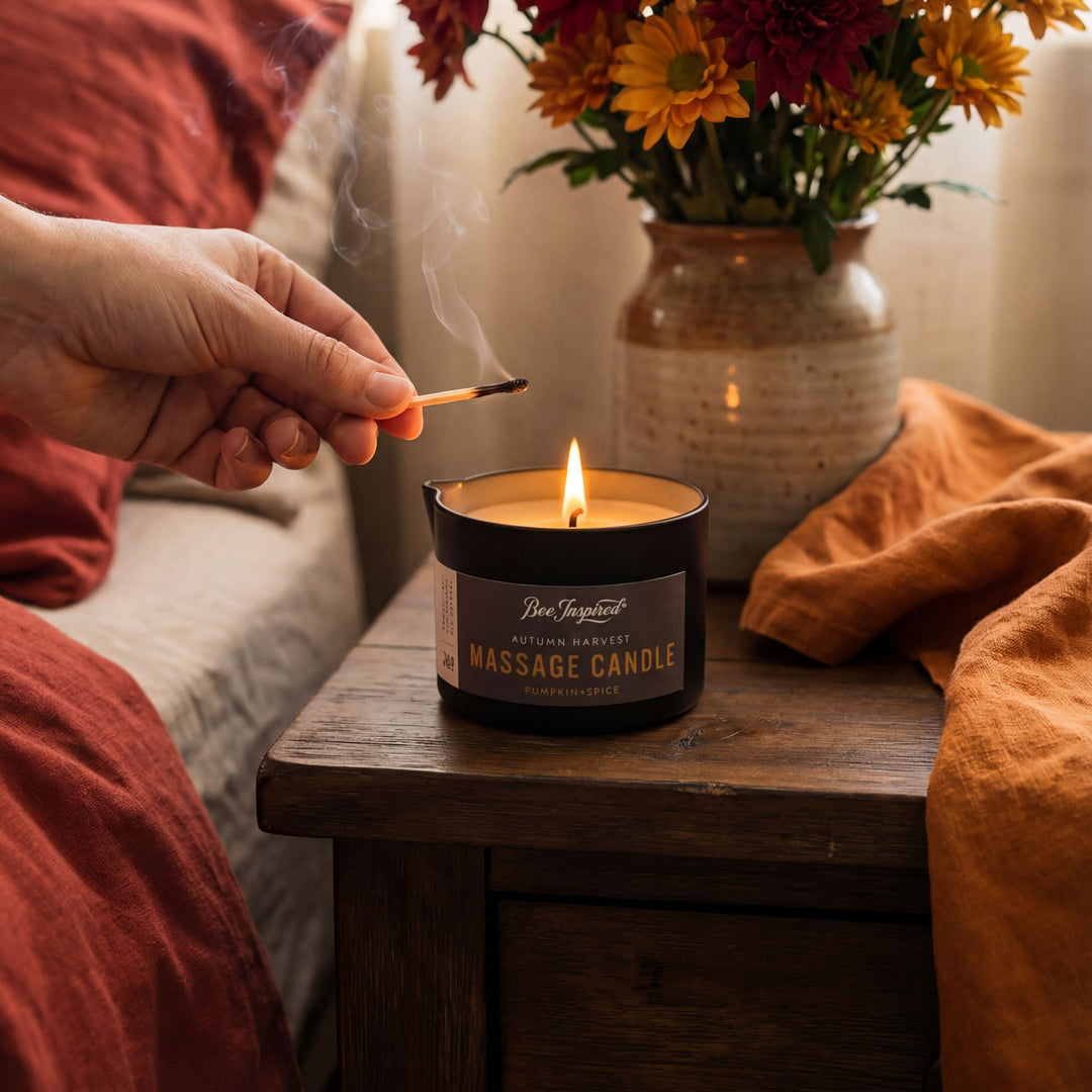 Person lighting a 'Massage Candle' with a vase of flowers in the background