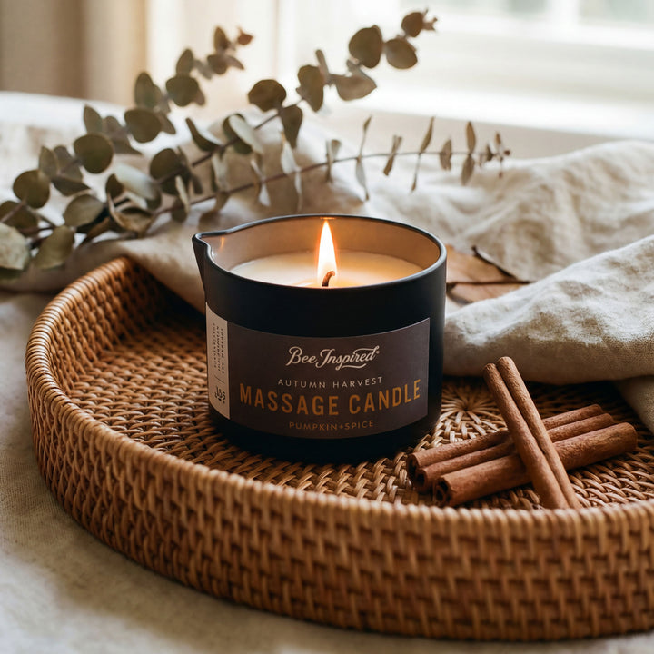 Lit massage candle on a woven tray with cinnamon sticks and eucalyptus leaves.