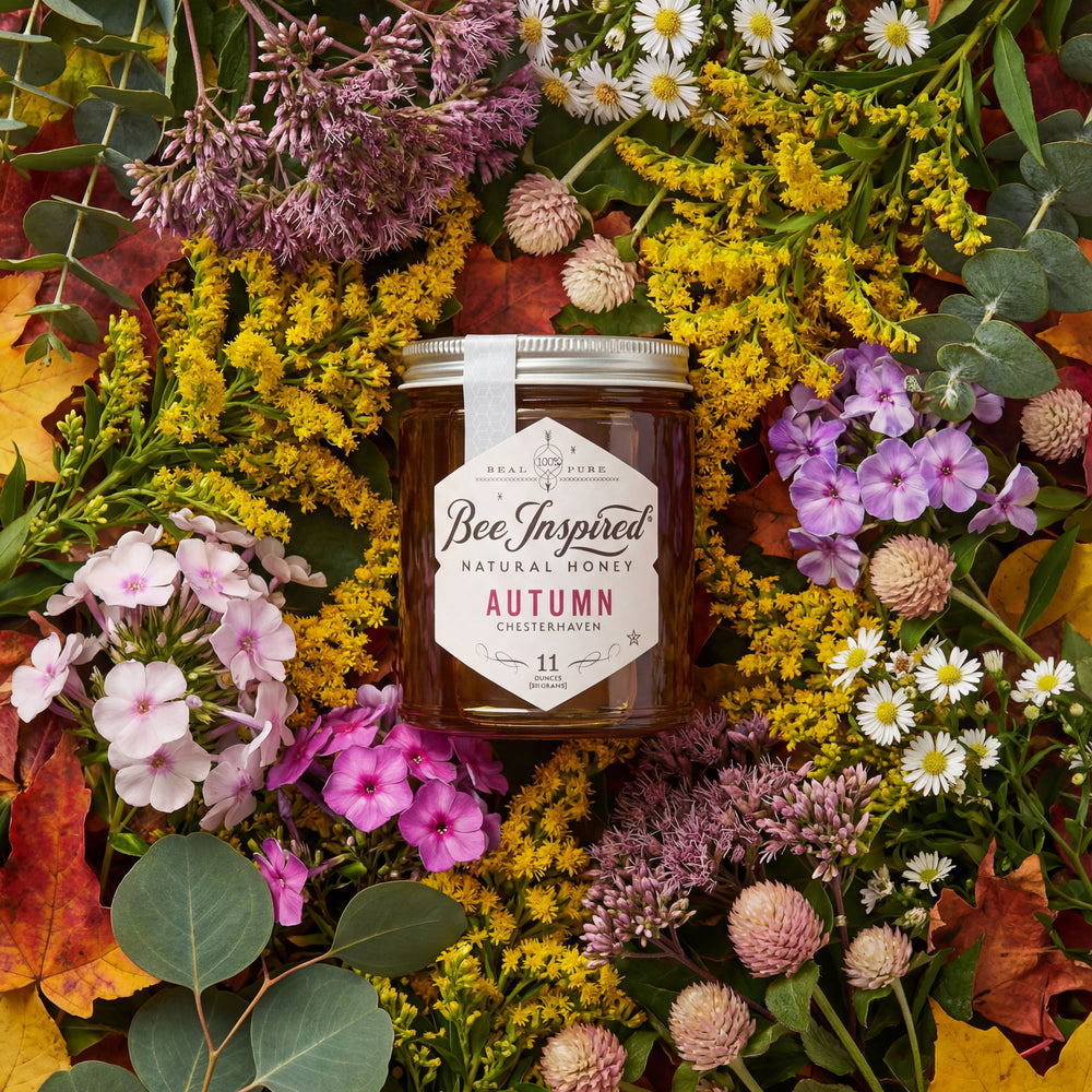 Jar of 'Bee Inspired' natural honey surrounded by autumn flowers and leaves