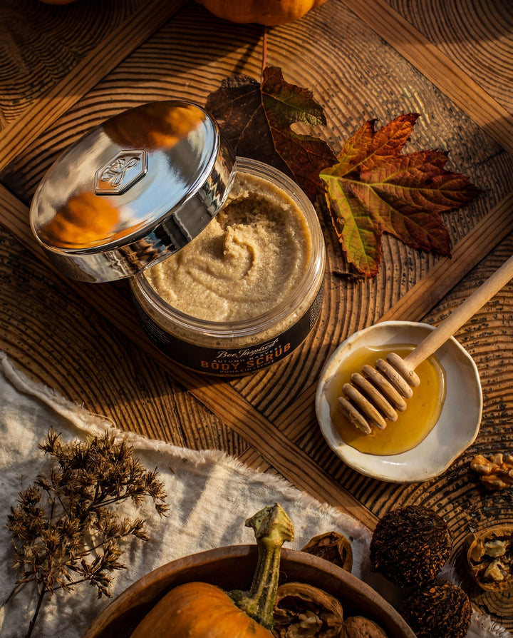 Jar of honey with a honey dipper on a wooden surface with autumn leaves and pumpkins.