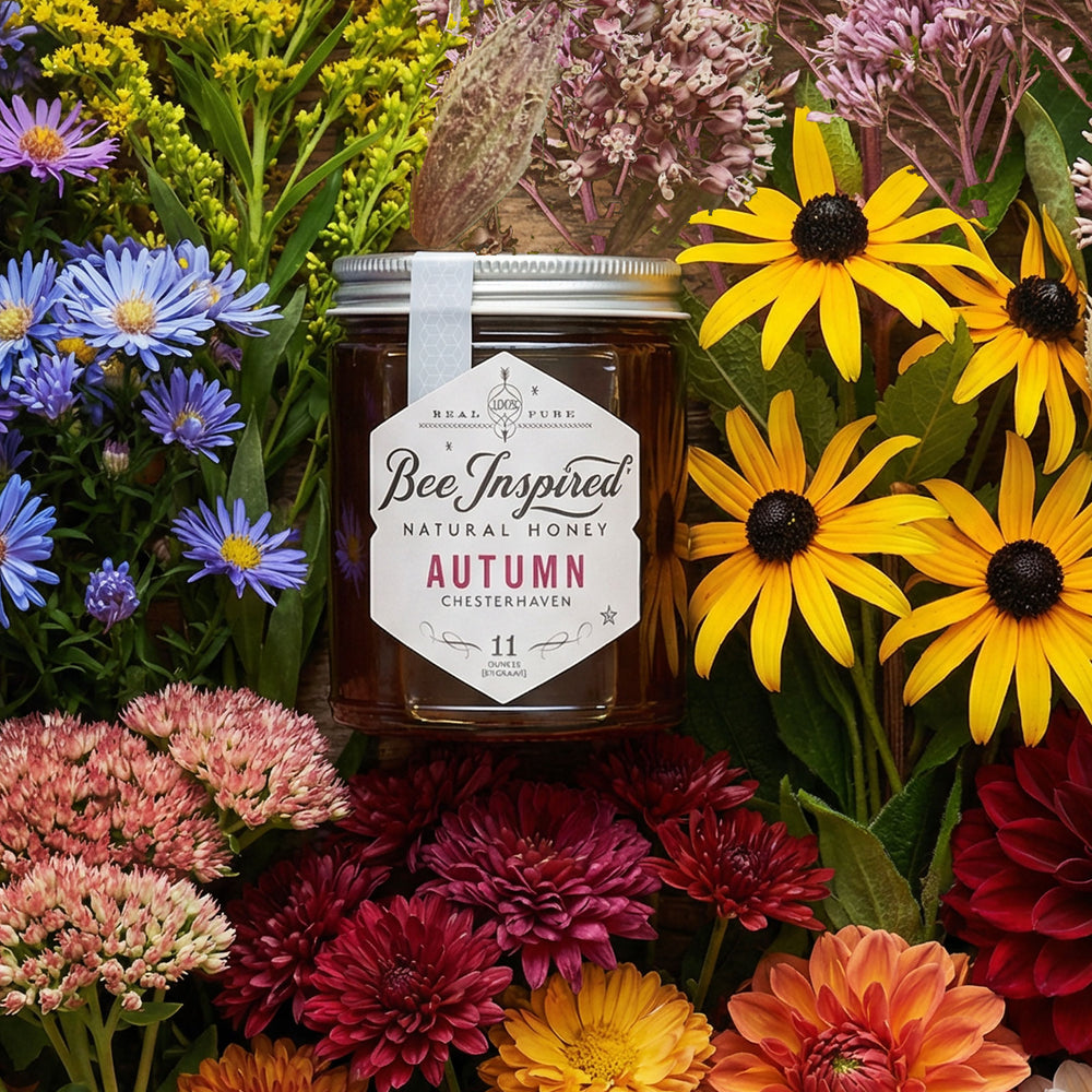 Jar of 'Bee Inspired' natural honey surrounded by a variety of colorful flowers