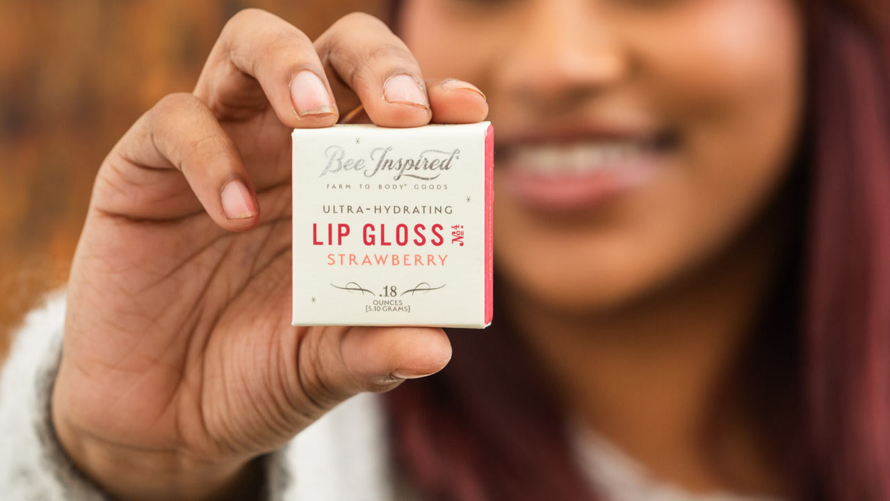 woman holding bee inspired strawberry lip gloss close to the camera