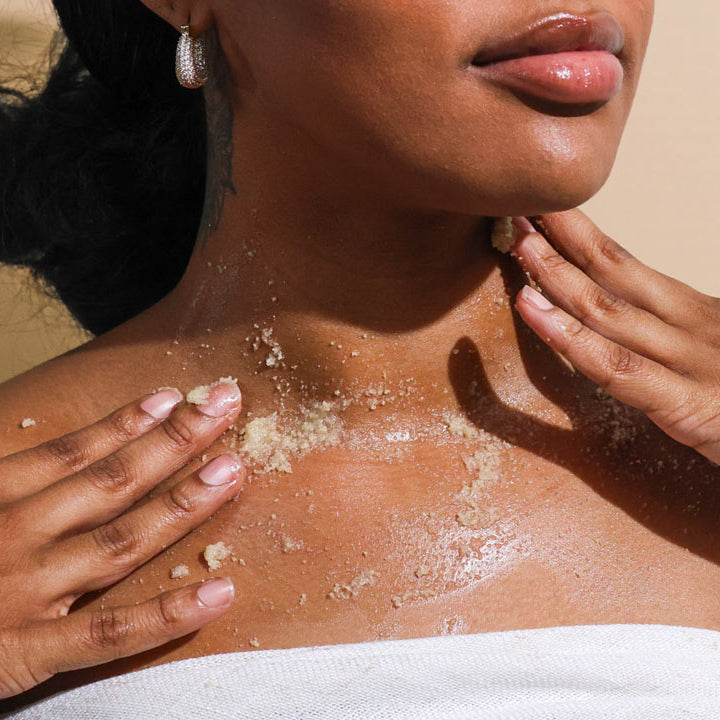 woman uses body scrub on her shoulders and chest