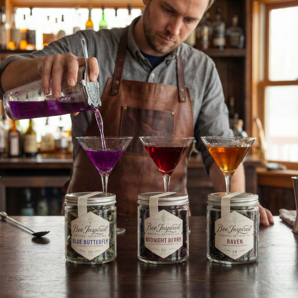 Barista pouring a purple liquid into a glass with jars labeled 'Bee Inspired' on a wooden counter.