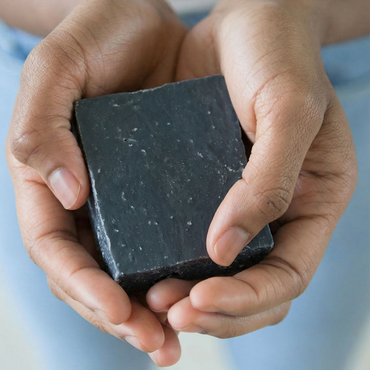 Hands holding a bar of black soap against a blurred background
