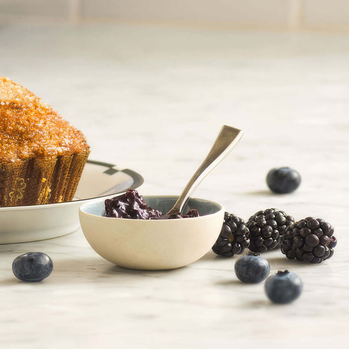 a bowl of jam with blueberries and blackberries next to a muffin