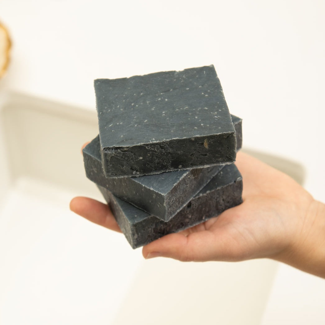 Hand holding a stack of black soap bars against a white background