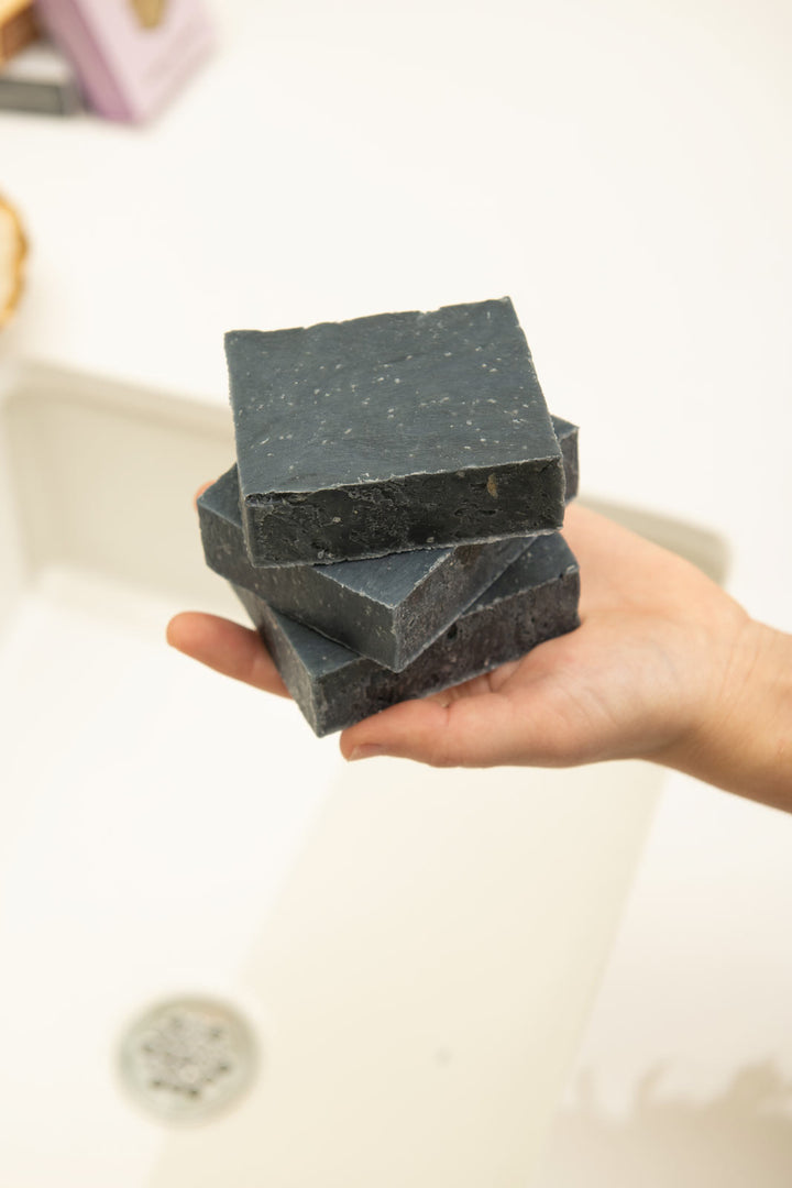 Person holding black clay bar soap stack over the sink 