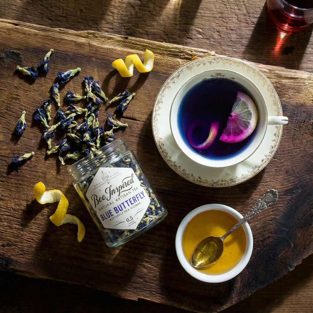 Tea leaves, a jar of 'Blue Butterfly' tea, and two cups of tea on a wooden surface.