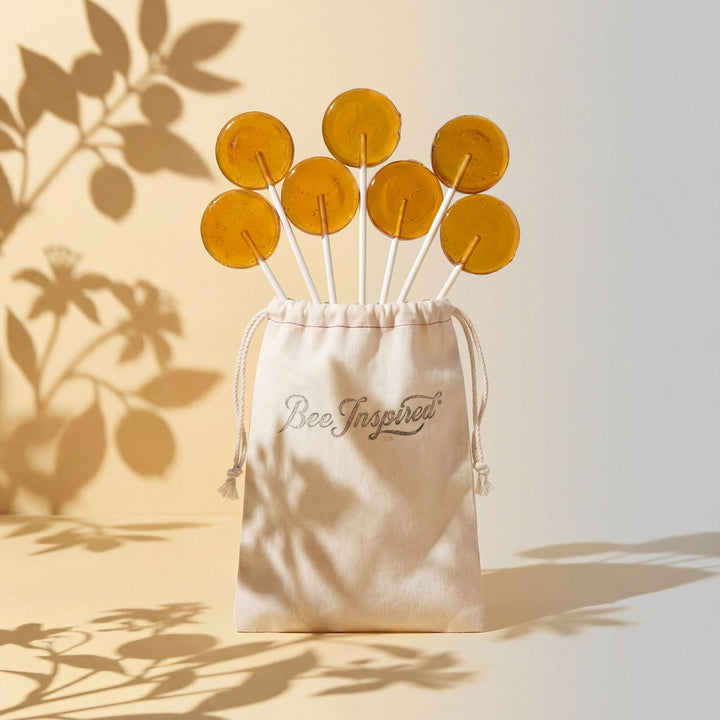 Bee-themed lollipops in a 'Bee Inspired' drawstring bag with leaf shadows on a light background