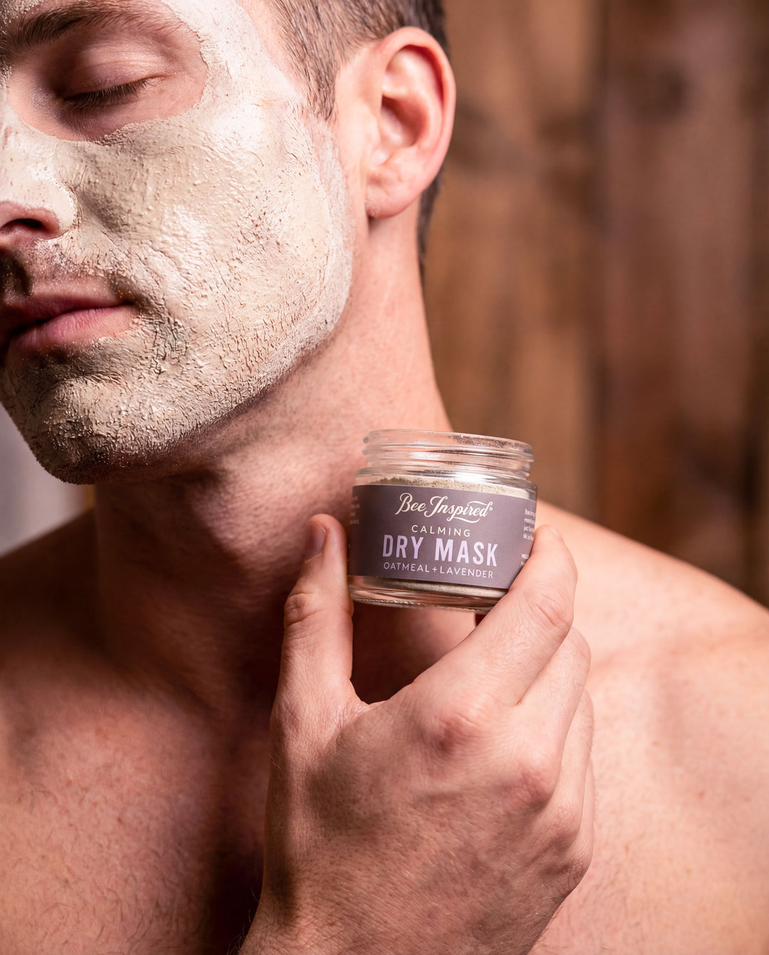 Man applying a dry mask to his face with a jar of the product in his hand.