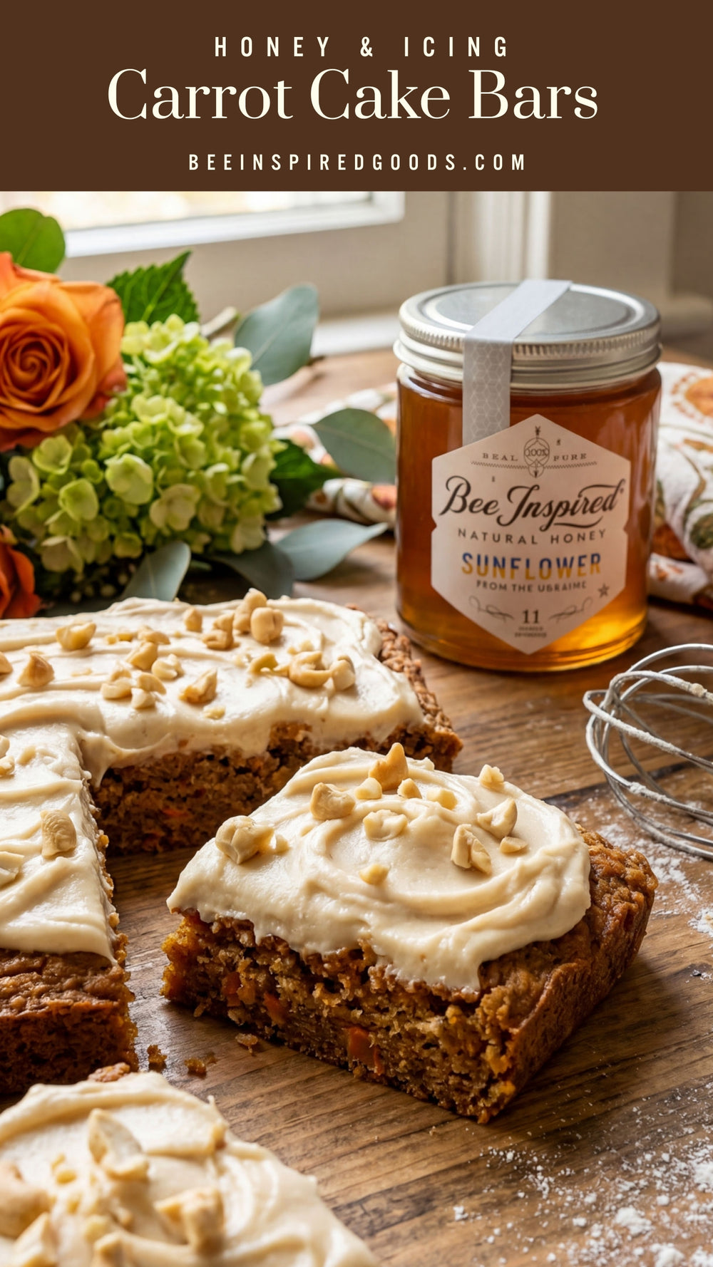 Carrot cake bars with icing on a wooden board, accompanied by a jar of honey and flowers.
