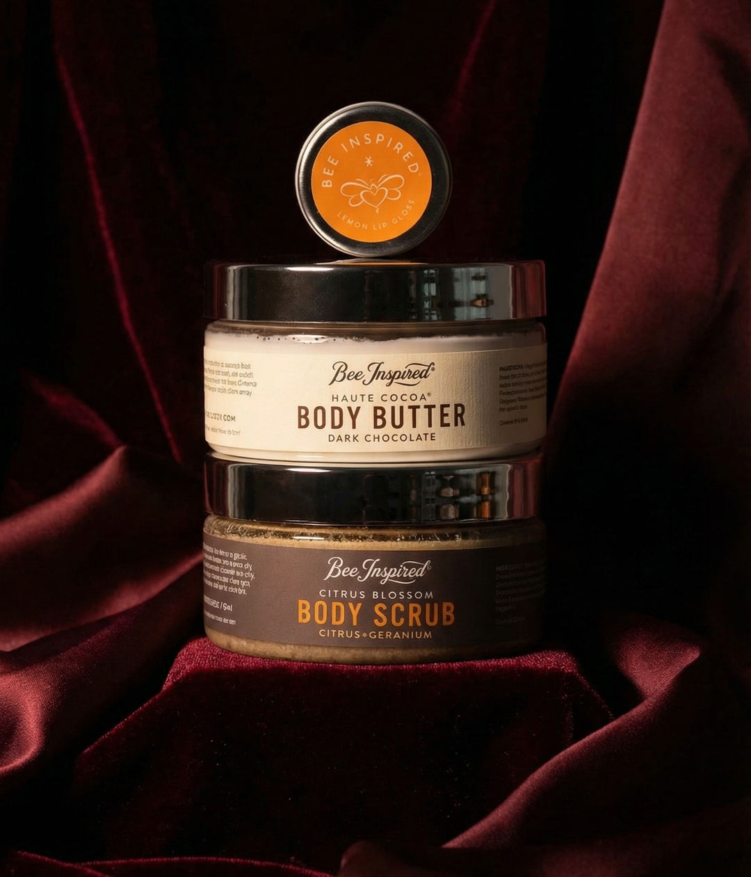 haute cocoa body butter and citrus blossom scrub and lemon lip gloss on dark red velvet background