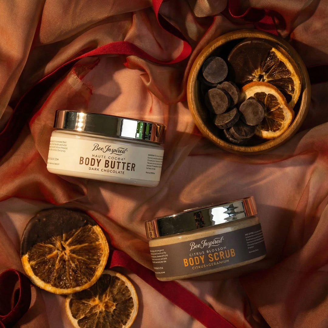 Two containers of Bee Inspired body products on a satin surface with dried oranges.