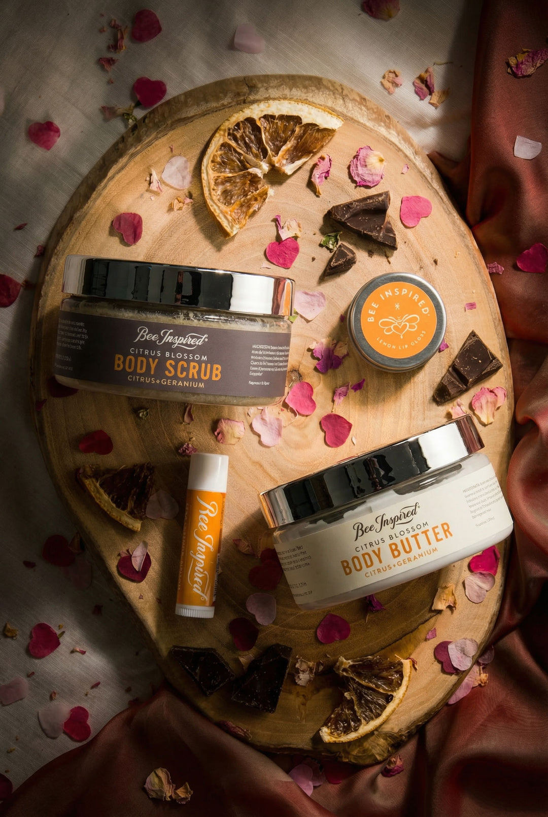 Body care products including body scrub, body butter, and lip balm on a wooden board with decorative elements.
