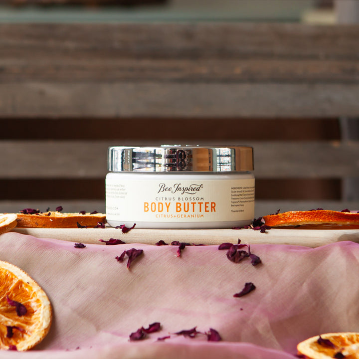 citrus body butter on table with flower petals and dried orange slices 