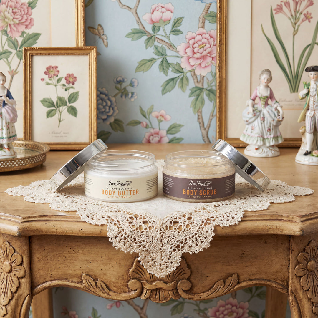 Two jars of body products on a decorative table with floral wallpaper in the background