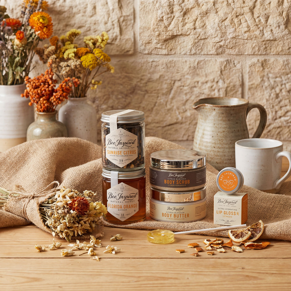 Bee Inspired body care products on a wooden surface with flowers and a stone wall background