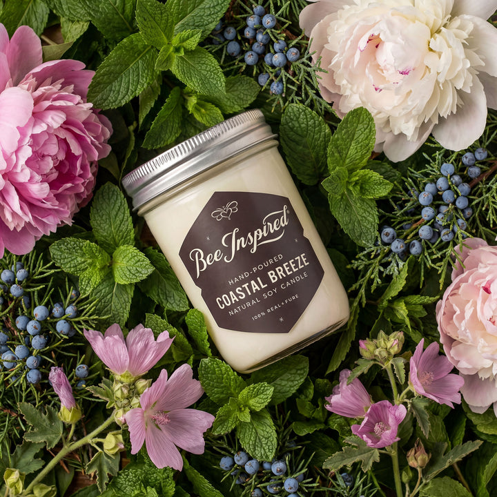 Candle labeled 'Bee Inspired' surrounded by flowers and greenery