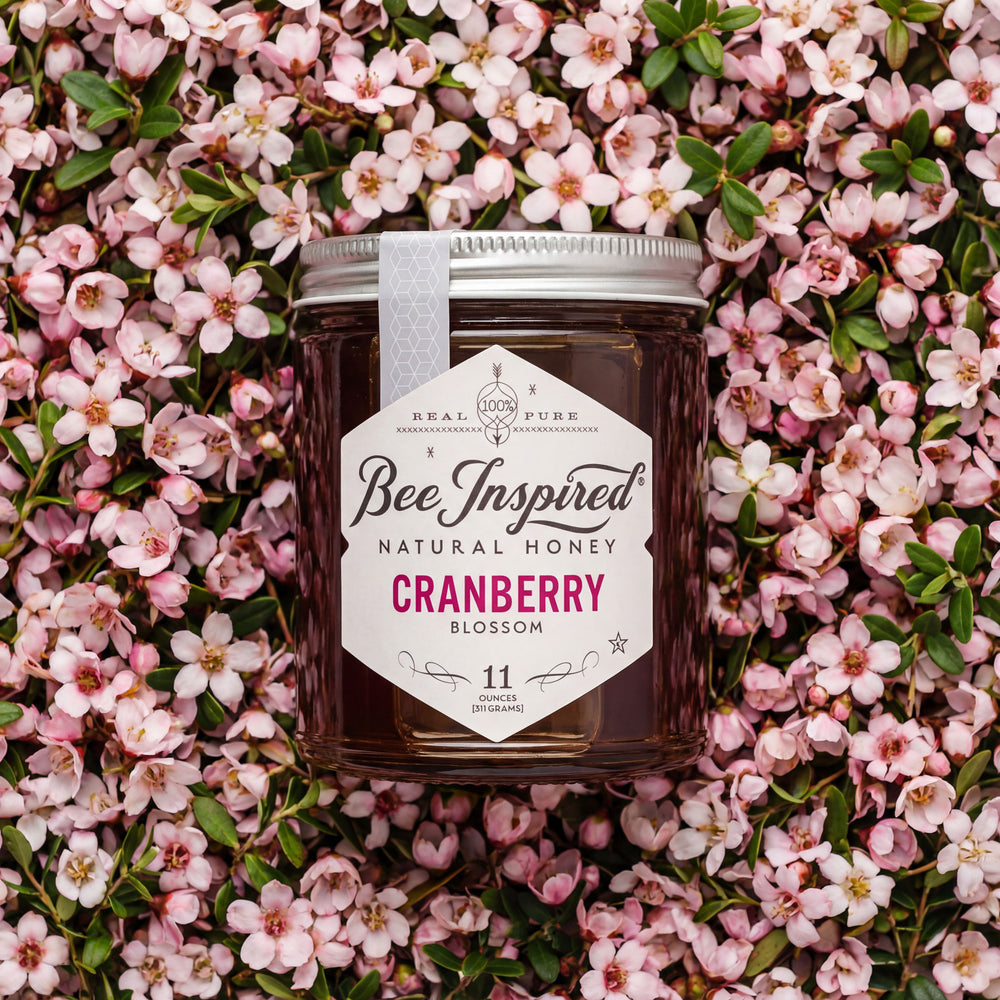 Jar of Bee Inspired Natural Honey Cranberry Blossom on a bed of pink flowers