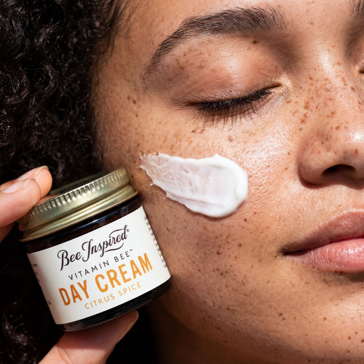 Person applying day cream to their face with a jar of Bee Inspired Vitamin Bee Day Cream.