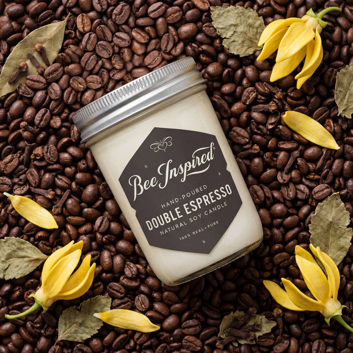 Candle jar labeled 'Bee Inspired' on a bed of coffee beans with yellow flowers and leaves.