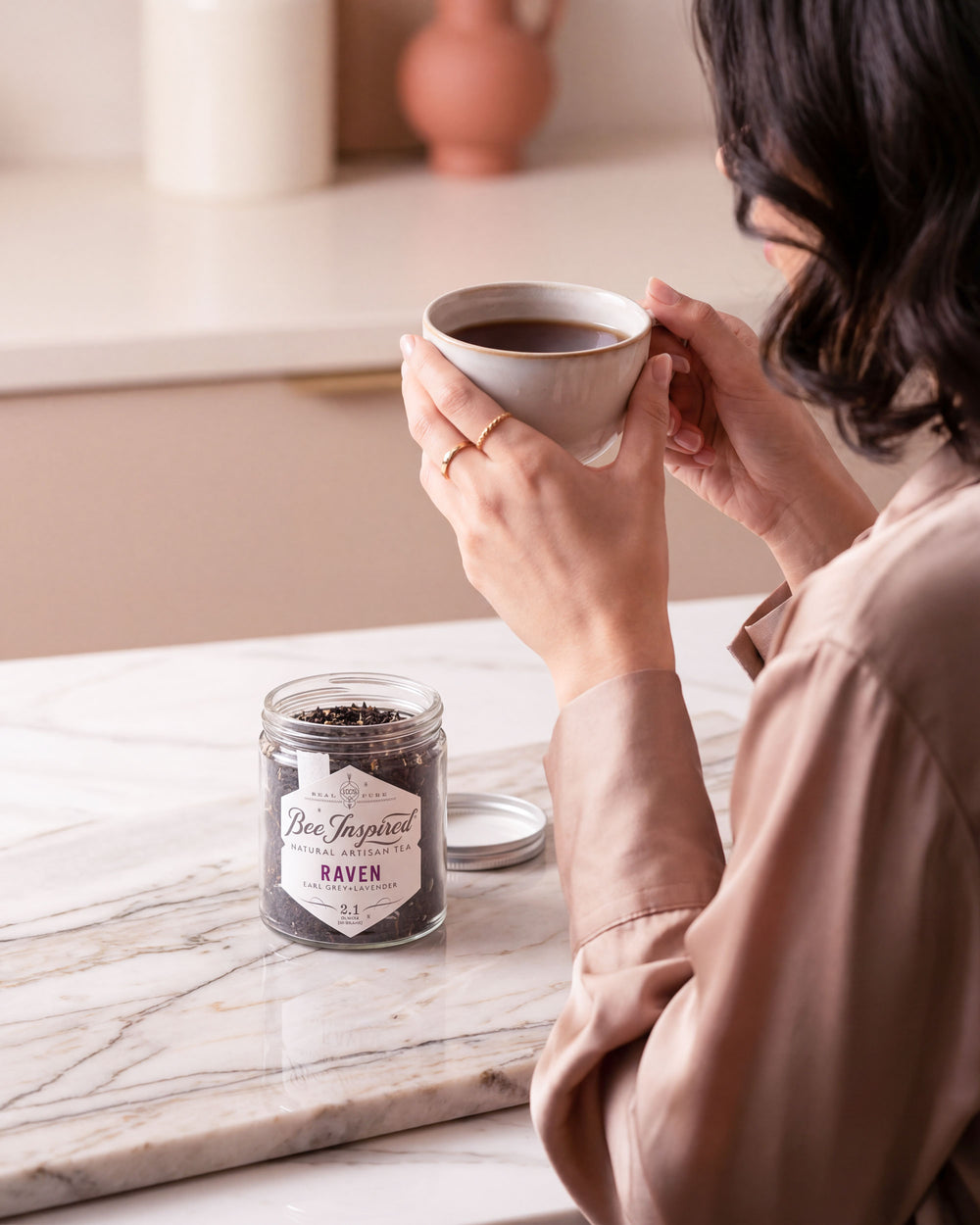 Person holding a coffee cup with a jar of coffee beans on a marble surface