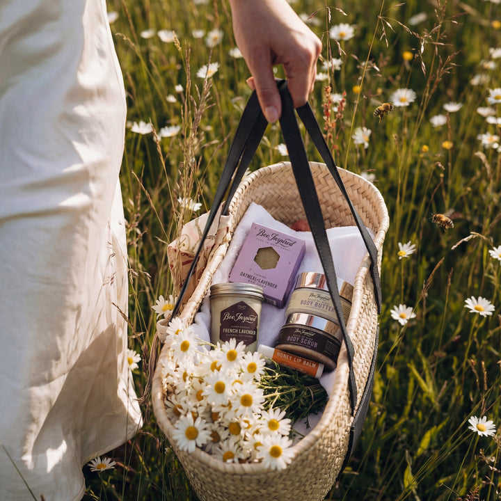 Person holding a woven basket with products and flowers in a field