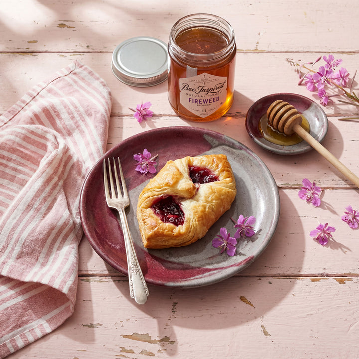 Pastries on a plate with a jar of honey and flowers on a wooden table